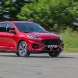 Czerwony Ford Kuga Hybrid w ruchu, z rozmytym tłem zieleni i drogi.
