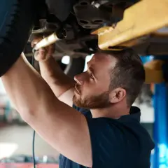 Mechanik sprawdza podwozie auta, by ustalić, ile kosztuje przegląd samochodowy.
