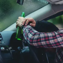 Pijany kierowca z butelką piwa w ręku. Za alkohol 1 promil prawo jazdy zabierają.