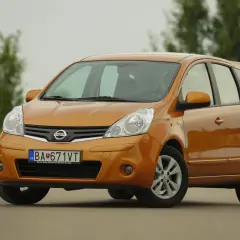 Pomarańczowy Nissan Note z przodu, na tle drzew.