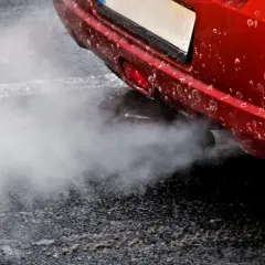 Z rury wydechowej czerwonego auta wydobywa się biały dym, jakby rozbiegany diesel próbował złapać oddech.