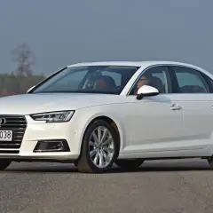 Białe Audi A4 sedan z kierowcą za kierownicą, zaparkowane na drodze.