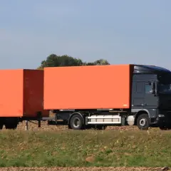 Ciemnoszary tir z pomarańczowymi naczepami jedzie przez pole. Zastanawiasz się, ile zarabia kierowca tira?