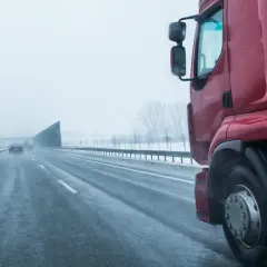 Czerwona ciężarówka na mokrej autostradzie w zimowy dzień. Kierowca zastanawia się, ile zarabia na godzinę, pokonując kolejne kilometry.