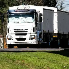 Biała ciężarówka Iveco z naczepą jedzie drogą. Kierowca ciężarówek wyrusza w długą trasę.