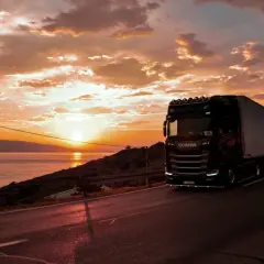 Ciężarówka Scania na drodze przy zachodzie słońca nad morzem. Zastanawiasz się, ile zarabia kierowca tira w Hiszpanii?