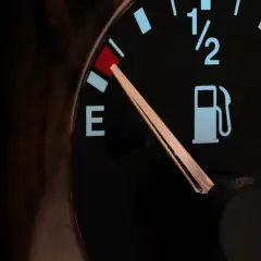 Wskaźnik paliwa w Toyocie Yaris pokazuje niski poziom. Czerwona lampka ostrzegawcza z ikoną dystrybutora paliwa świeci się, a wskazówka na wskaźniku znajduje się blisko litery "E", sygnalizując niski **pojemność baku**.