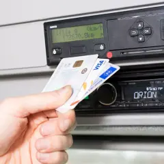 Dłoń wkłada kartę kierowcy do tachografu. Widoczny slot na kartę i ekran urządzenia.