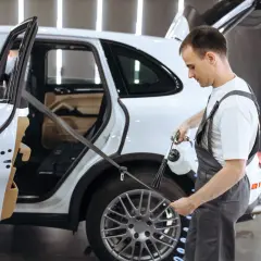 Pracownik detailingu samochodowego pokazuje, jak prać pasy bezpieczeństwa w białym SUV-ie, używając specjalistycznego sprzętu.