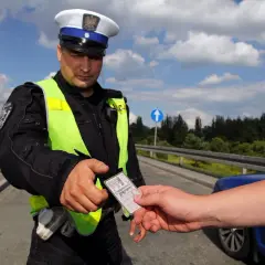 Policjant w kamizelce odblaskowej odbiera dokument. Czy trzeba mieć przy sobie prawo jazdy? Tak, podczas kontroli drogowej.