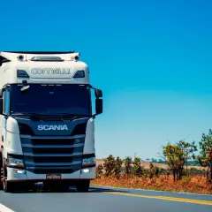Biała ciężarówka Scania z naczepą jedzie po pustej drodze. Kierowca c. zarabia na życie, przewożąc towary.