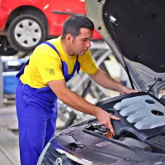 Mechanik w żółtej koszulce i niebieskich ogrodniczkach sprawdza silnik. Zastanawiasz się, ile zarabia kierowca mechanik?