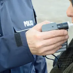 Policjant w mundurze z napisem "POLICJA" trzyma alkomat, a kobieta dmucha w jego ustnik. To przykład, jak dmuchać w alkomat.