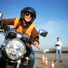 Uśmiechnięta kursantka na motorze, w kamizelce odblaskowej i kasku, uczy się jeździć. Zastanawiasz się, ile kosztuje prawo jazdy na motor?