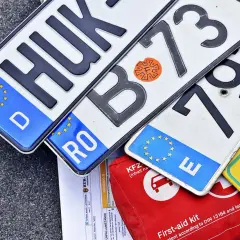 Niemieckie, rumuńskie i inne tablice rejestracyjne państw UE leżą obok apteczki.