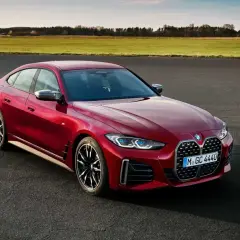 Czerwone BMW Gran Coupe na tle zielonych pól i błękitnego nieba. Elegancka linia nadwozia i sportowe felgi podkreślają dynamiczny charakter tego auta.