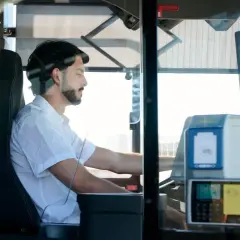 Mężczyzna za kierownicą autobusu, zastanawiający się, ile zarabia kierowca autobusu. Widoczny biletomat i siedzenie kierowcy.