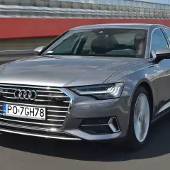 Szary sedan Audi A6 jedzie po drodze, widoczny przód i bok.