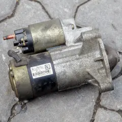 Rozrusznik samochodowy, kluczowy element do uruchomienia silnika. Widać jego metalową obudowę i złącza.