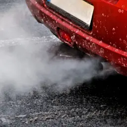 Z rury wydechowej czerwonego auta wydobywa się biały dym, jakby rozbiegany diesel próbował złapać oddech.