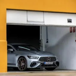 Srebrne coupe auto AMG GT 4-drzwiowe z brązowymi felgami stoi w garażu z żółtą ścianą.