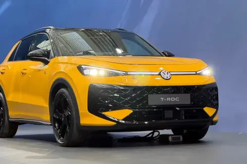 Żółty Volkswagen T-Roc z czarnym dachem i felgami. Zbliżenie na przód auta, widoczne światła LED i atrapa chłodnicy.
