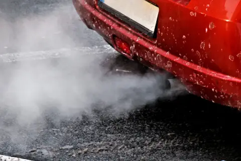 Z rury wydechowej czerwonego auta wydobywa się biały dym, jakby rozbiegany diesel próbował złapać oddech.