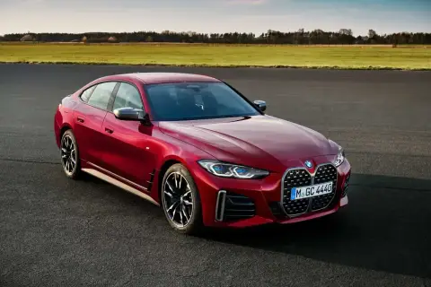 Czerwone BMW Gran Coupe na tle zielonych pól i błękitnego nieba. Elegancka linia nadwozia i sportowe felgi podkreślają dynamiczny charakter tego auta.
