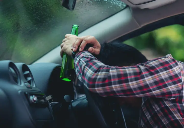 Pijany kierowca z butelką piwa w ręku. Za alkohol 1 promil prawo jazdy zabierają.
