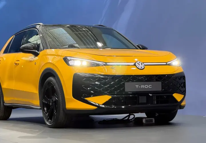 Żółty Volkswagen T-Roc z czarnym dachem i felgami. Zbliżenie na przód auta, widoczne światła LED i atrapa chłodnicy.