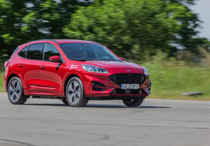 Czerwony Ford Kuga Hybrid w ruchu, z rozmytym tłem zieleni i drogi.