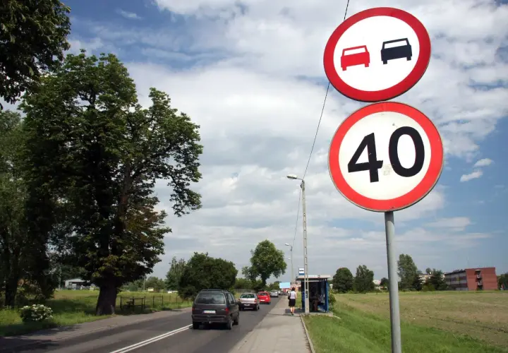 Znaki drogowe: zakaz wyprzedzania i ograniczenie prędkości do 40 km/h. Samochody jadą drogą, po prawej stronie przystanek autobusowy.