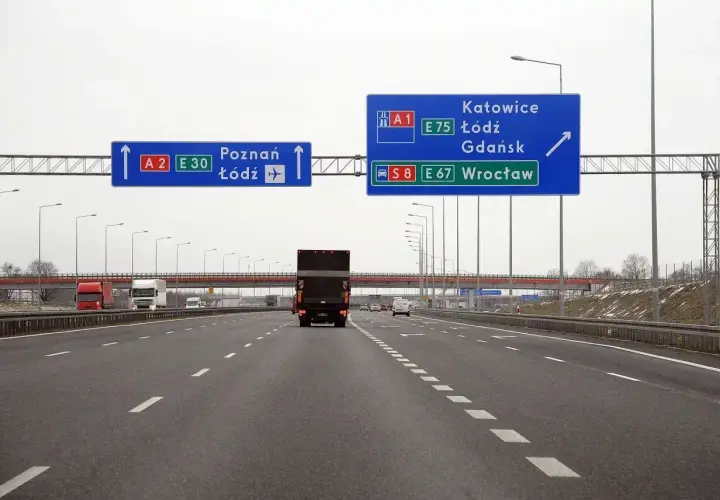 Autostrada z niebieskimi znakami drogowymi wskazującymi kierunki: Poznań, Łódź, Katowice, Gdańsk, Wrocław.