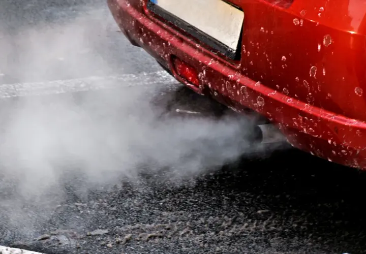 Z rury wydechowej czerwonego auta wydobywa się biały dym, jakby rozbiegany diesel próbował złapać oddech.