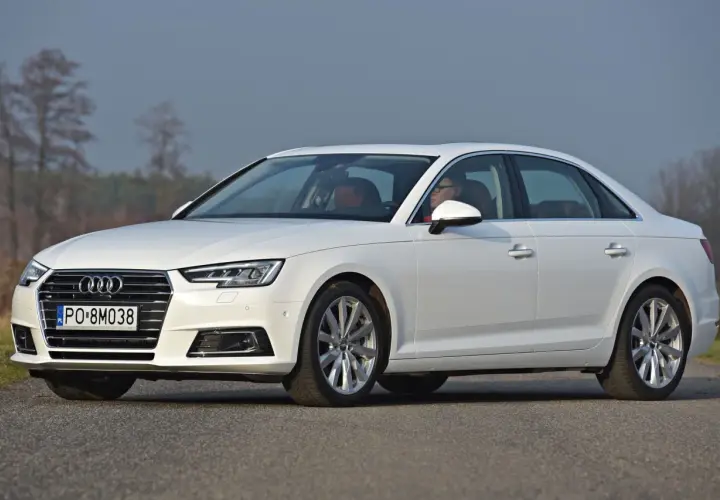 Białe Audi A4 sedan z kierowcą za kierownicą, zaparkowane na drodze.