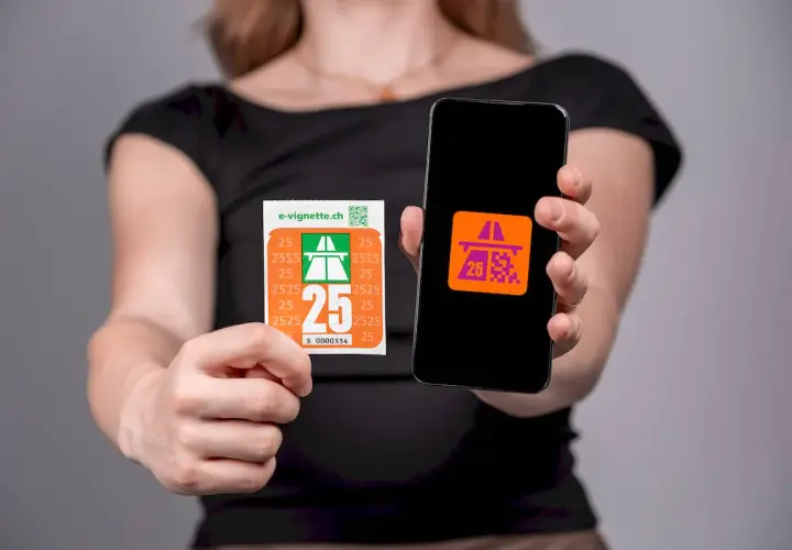 Kobieta pokazuje naklejkę i ekran telefonu z symbolem autostrady, symbolizującym winietę szwajcaria.