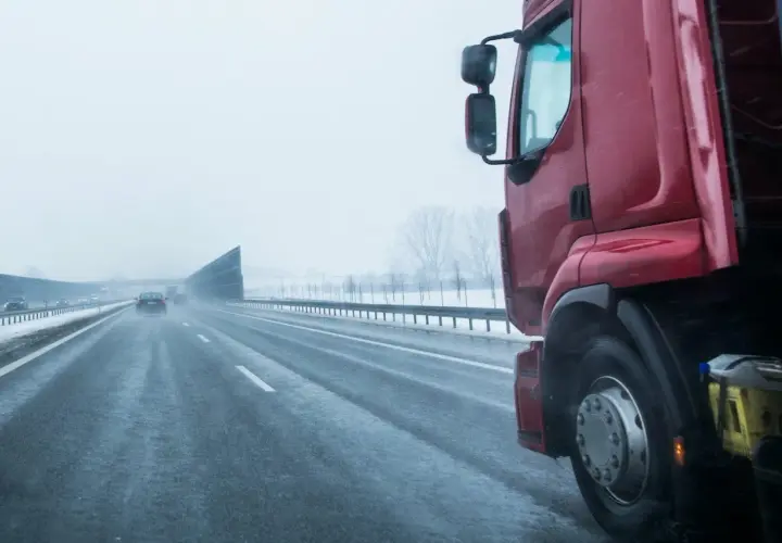 Czerwona ciężarówka na mokrej autostradzie w zimowy dzień. Kierowca zastanawia się, ile zarabia na godzinę, pokonując kolejne kilometry.
