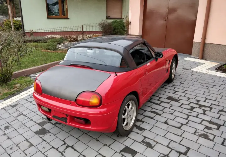 Czerwone Suzuki Cappuccino z czarnym dachem i maską stoi na podjeździe z kostki brukowej.