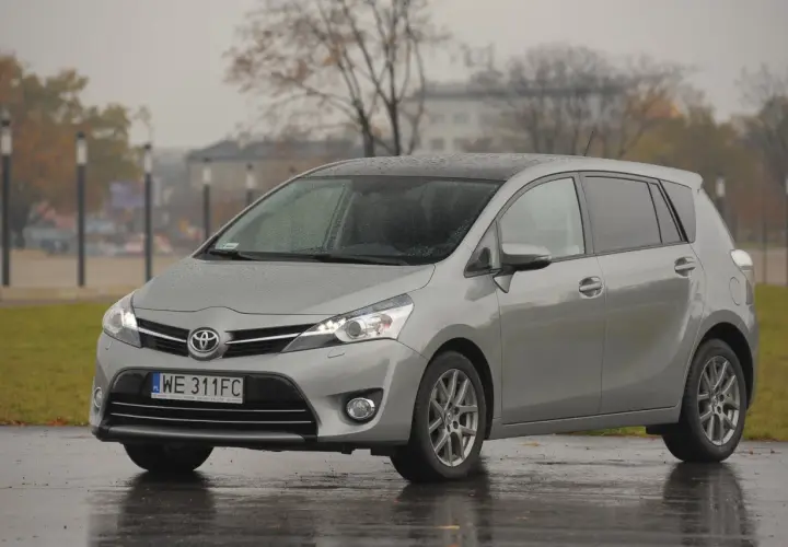 Srebrny minivan Toyota Verso zaparkowany na mokrej nawierzchni w deszczowy dzień.