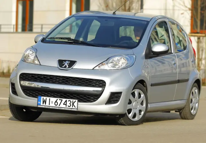 Srebrny Peugeot 107 z przodu, widoczny kierowca.