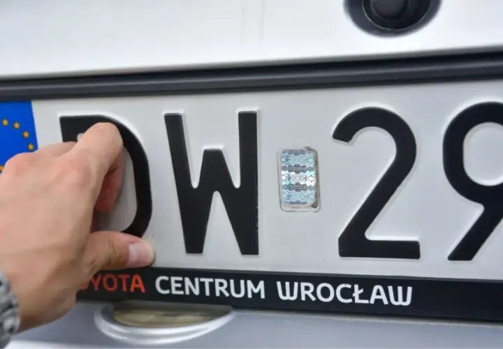 Dłoń poprawia hologram na tablicy rejestracyjnej DW 29. Toyota Centrum Wrocław.