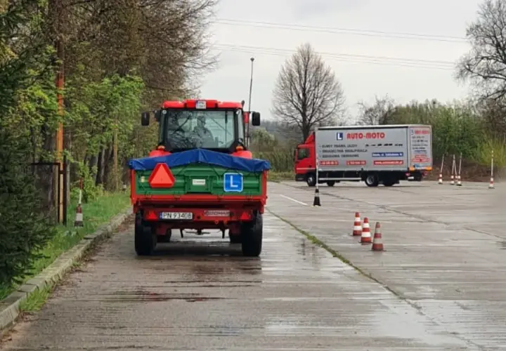 Czerwony traktor z przyczepą na placu manewrowym, obok ciężarówka AUTO-MOTO.