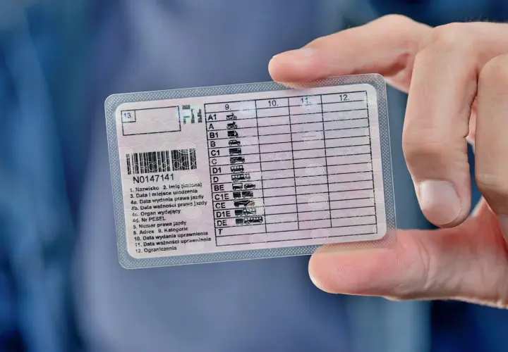Dłoń trzyma polskie prawo jazdy, na którym widnieje numer N0147141. Dokument zawiera informacje o kategoriach pojazdów i datach ważności, kluczowych dla przedłużenia prawa jazdy.