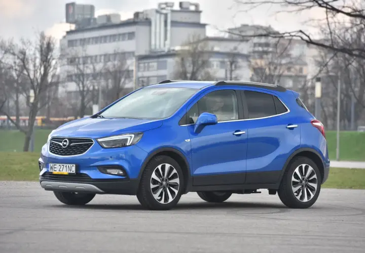 Niebieski Opel Mokka stoi na drodze, w tle budynki i drzewa.