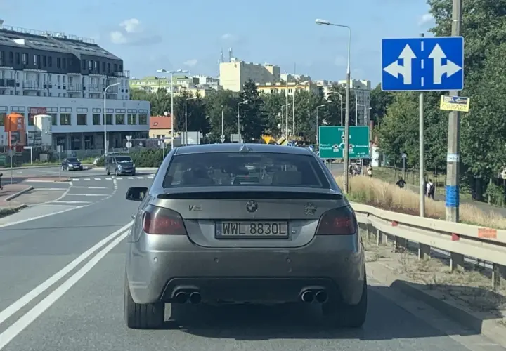 Szare BMW z rejestracją WWL 8830L na drodze, w tle budynki i znaki drogowe.