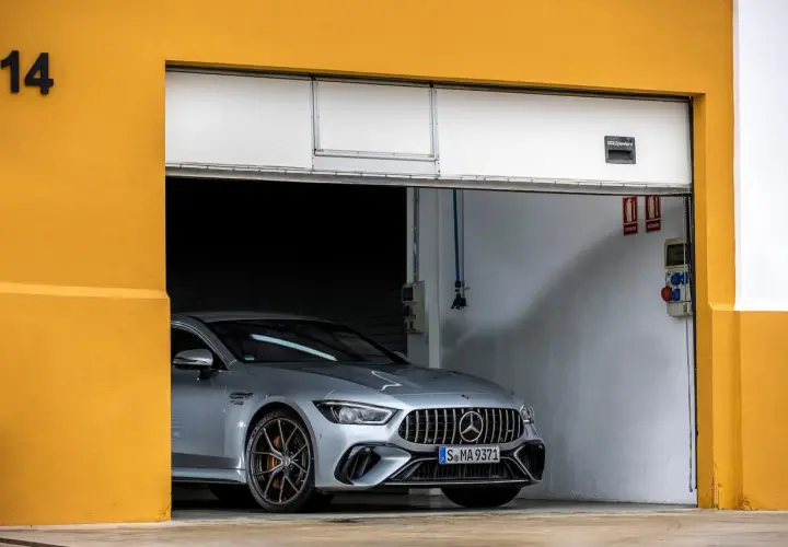 Srebrne coupe auto AMG GT 4-drzwiowe z brązowymi felgami stoi w garażu z żółtą ścianą.