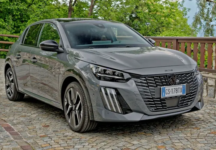Szary Peugeot 208 zaparkowany na brukowanej drodze, z zielenią w tle.