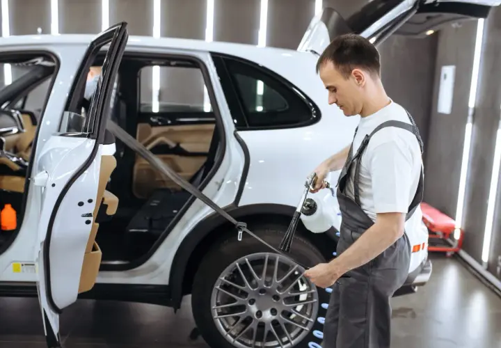 Pracownik detailingu samochodowego pokazuje, jak prać pasy bezpieczeństwa w białym SUV-ie, używając specjalistycznego sprzętu.