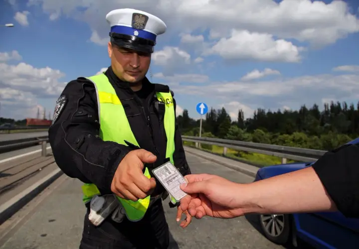 Policjant w kamizelce odblaskowej odbiera dokument. Czy trzeba mieć przy sobie prawo jazdy? Tak, podczas kontroli drogowej.