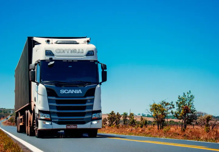 Biała ciężarówka Scania z naczepą jedzie po pustej drodze. Kierowca c. zarabia na życie, przewożąc towary.